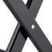 A close-up of a black Lancaster Table & Seating wood folding luggage rack with an x-shaped base.