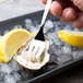 A hand holding an Arcoroc stainless steel oyster fork over an oyster on ice.