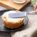 A person using a Chef & Sommelier stainless steel butter spreader to spread butter on a piece of bread.