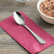 A Choice Milton stainless steel teaspoon on a pink napkin next to a bowl of chocolate pudding.
