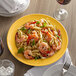 A Tuxton Concentrix saffron china plate with pasta, shrimp, and basil on a table.