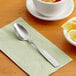 A Choice stainless steel teaspoon on a napkin next to a cup of tea and lemon slices.