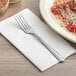 A Choice Dominion stainless steel dinner fork on a napkin next to a plate of pasta.