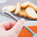 A hand holding a World Tableware stainless steel bouillon spoon over a bowl of soup.