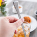A hand holding a Libbey stainless steel iced tea spoon in a glass of ice.