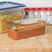 A Carlisle amber plastic food pan filled with pasta on a kitchen counter.