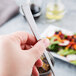 A hand using a Libbey stainless steel iced tea spoon to stir a drink in a glass of salad