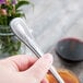 A hand holding a Libbey stainless steel dessert spoon.