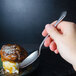 A hand holding a World Tableware stainless steel dessert spoon over a dessert.