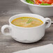 A white Schonwald two-handled soup cup filled with soup on a table with a bowl of salad.