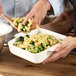 A hand holding a Villeroy & Boch white porcelain square serving dish full of pasta and broccoli.