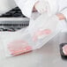 A person in white gloves using a Galaxy VME1 vacuum packaging machine to seal a bag of meat.