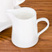 A close up of a white CAC porcelain creamer filled with milk.