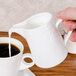 A person pouring milk into a white mug of coffee.