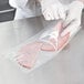 A person in gloves using a VacPak-It plastic bag to vacuum package a piece of ham.