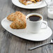 A white porcelain cup of coffee and a plate of croissants on a table.