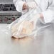 A person in a white coat using a VacPak-It chamber vacuum packaging bag to package a chicken.