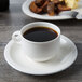 A cup of coffee on a white porcelain saucer with food.
