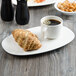 A Villeroy & Boch white porcelain stackable cup filled with coffee on a saucer with a croissant.