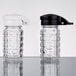 Two Tablecraft clear glass shakers with white and black lids.