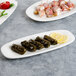 A Villeroy & Boch white porcelain oval platter with stuffed grape leaves, lemon wedges, and skewers on a white table.