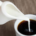 A white pitcher pouring milk into a cup of coffee.