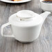 A white Villeroy & Boch porcelain teapot on a wood table with a cup of coffee.