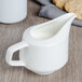 A white Villeroy & Boch porcelain creamer on a table with a cookie.