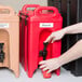 A person's hand pushing a red Cambro Camtainer with black accents.