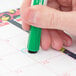 A person using an Expo fine point green magnetic dry erase marker to write on a calendar.