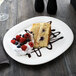 A Villeroy & Boch white porcelain oval platter with a slice of cake topped with whipped cream and berries on a table.