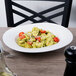 A Villeroy & Boch white porcelain oval bowl filled with pasta with cheese and tomatoes on a table with a fork and plate.
