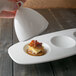 A hand holding a white porcelain bell cover over a small plate of food.