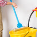 A person holding an Impact 12 3/4" Sponge Mop and yellow bucket.