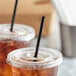 Two plastic cups of iced tea with Choice black wrapped straws on a table.