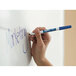 A hand writing "Expo Blue Low-Odor" in blue on a white board with an Expo fine point dry erase marker.