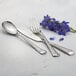 A Mikayla stainless steel dinner spoon on a table with silverware and a flower.