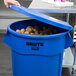 A hand holding a blue Rubbermaid BRUTE trash can full of potatoes.