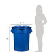 A woman standing in a room next to a blue Rubbermaid BRUTE trash can.