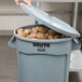 A person putting potatoes in a Rubbermaid BRUTE gray trash can.