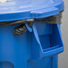 A blue Rubbermaid BRUTE trash can with a black lid and plastic bag inside.