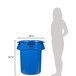 A woman standing next to a blue Rubbermaid BRUTE trash can with a lid.