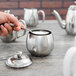 A hand holding a spoon over a silver sugar bowl.