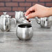 A hand using a silver Vollrath sugar bowl lid to pour sugar into a cup.