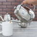 A hand pouring coffee into a silver Vollrath Orion teapot.