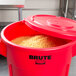 A red Rubbermaid BRUTE 55 gallon trash can with a lid full of food.