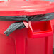 A red Rubbermaid BRUTE trash can with a black plastic bag around it.