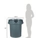 A woman standing next to a large grey Rubbermaid trash can.