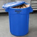 A blue trash can full of potatoes with a lid.