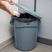 A woman in a corporate office putting a white plastic bag in a Rubbermaid BRUTE trash can.
